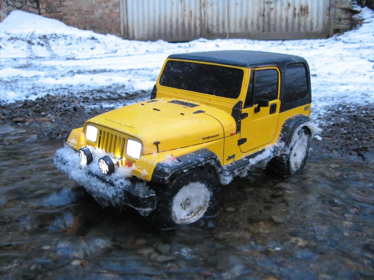 A Tamiya Jeep Wrangler YJ model in a shallow stream.